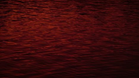 Abstract-red-sunset-dusk-reflection-on-rippling-lake-water,-slow-motion