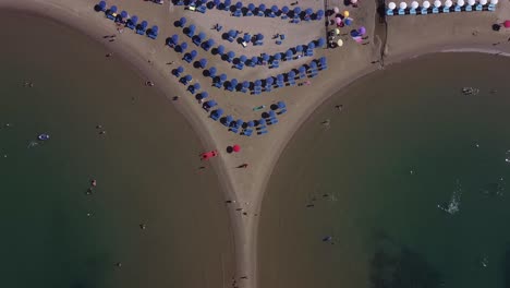 Stone-breakwater-and-lines-of-sunbed-with-umbrellas-on-Italy-coastline,-top-down