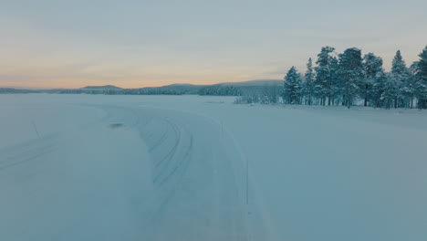 Aerial-view-following-Norbotten-driver-drifting-on-frozen-Lapland-ice-lake-in-sunrise-snow