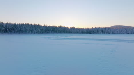 Norbotten-Swedish-Lapland-Polar-circle-ice-lake-and-woodland-aerial-view-towards-glowing-sunrise-skyline