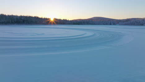 Norbotten-ice-track-curves-aerial-view-flying-over-alpine-snow-covered-woodland-during-golden-sunrise