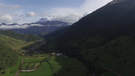 Aerial-Flying-Through-Green-Valley-With-Snow-Capped-Mountain-In-Distance