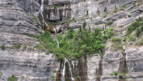 Backward-aerial-of-Bridal-Veil-Falls-from-steep-brown-majestic-mountains-in-Utah,-Provo-Canyon