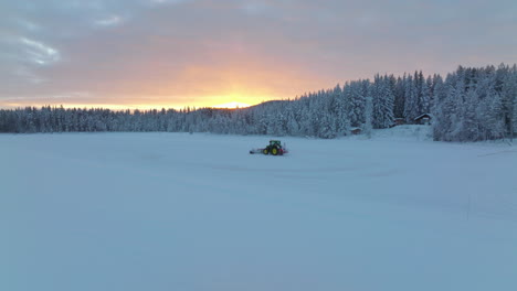 Tracking-Norbotten-tractor-snow-blower-clearing-woodland-ice-track-under-glowing-sunrise-aerial-view