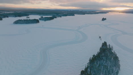 Snowy-Norbotten-ice-lake-track-course-formed-around-Lapland-woodland,-Sunrise-aerial-view
