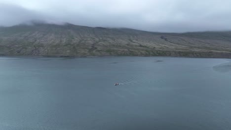 Luftaufnahme-über-Ein-Kleines-Fischerboot,-Das-Im-Faskrudsfjordur-Fjord-In-Ostisland-Unterwegs-Ist---Drohnenaufnahme