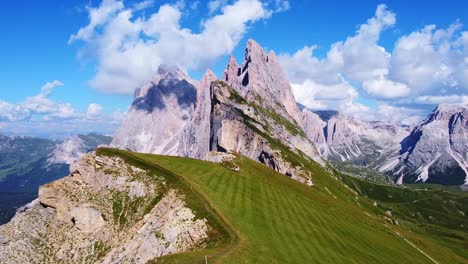 Flying-in-Aerial-view-of-the-peaks-of-Seceda-with-green-pastures,-and-hiking-trails-in-the-foreground,-and-mountain-peaks-in-the-background-in-the-Italian-Dolomites-in-South-Tyrol,-Italy