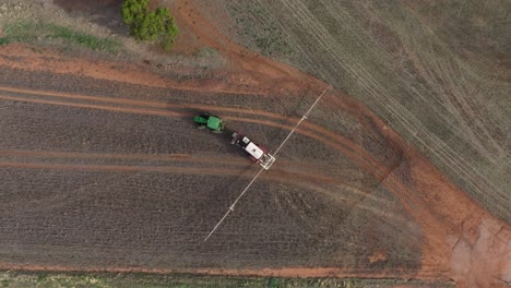 Top-down-shot-of-farming-tractor-towing-machinery-driving-across-field
