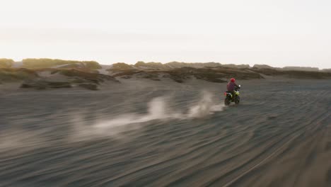 Person-riding-his-dirt-bike-bike-through-the-desert-during-sunrise,-scenic-drone-shot-zooming-in-with-copy-space