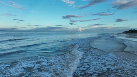 Very-low-angle-shot-of-Ocean-waves-on-Gold-Coast-Beach-at-sunset,-with-sandy-beach-and-blue-wavy-water,-flying-backwards
