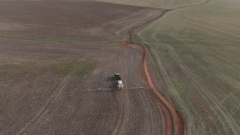 Drone-shot-panning-downwards-looking-at-farming-tractor-driving-across-hilly-field