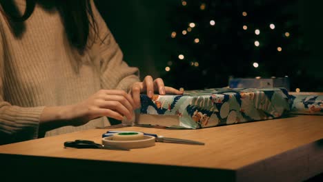 Frau-Verpackt-Ein-Weihnachtsgeschenk,-Geschmückter-Baum-Blinkt-Im-Hintergrund