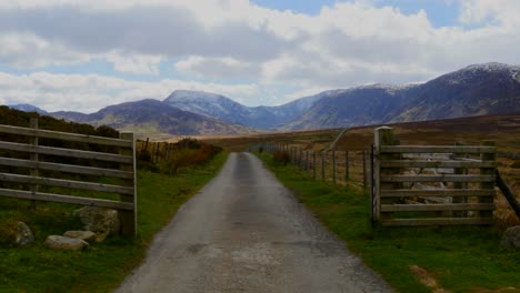 Camera-Tracks-across-an-open-gate-with-a-country-road-leading-to-the-mountains-of-Wales-in-the-UK