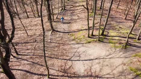 Man-cycling-through-an-outdoor-trail-in-the-middle-of-the-woods-during-a-sunny-day,-aerial-drone-shot