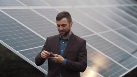 Satisfied-handsome-man-in-a-jacket-pulls-out-a-wad-of-money-against-the-background-of-a-solar-power-plant