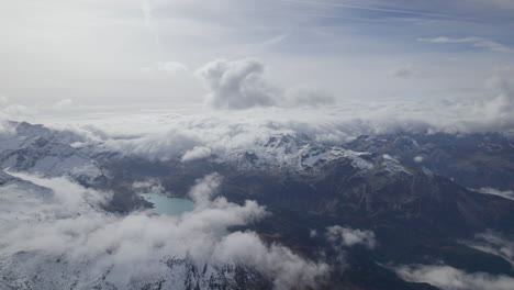 Hochwinkel-Drohne,-Die-An-Sonnigen-Tagen-über-Den-Wolken-Geschossen-Wurde-Und-Schneebedeckte-Gipfel-Der-Berge-In-Österreich-Zeigt---Blauer-See-Im-Tal