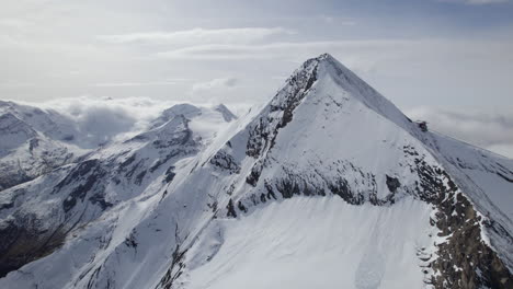 Cinematic-drone-shot-of-snowy-mountain-summit-during-sunny-day-in-austrian-Alps