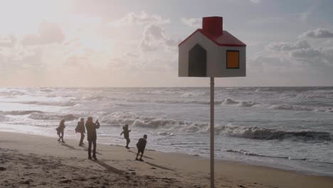 Silhouette-Einer-Glücklichen-Familie,-Die-Mit-Dem-Wind-Am-Strand-Spielt,-Mit-Einem-Orientierungsstab-Im-Vordergrund---De-Haan,-Belgien