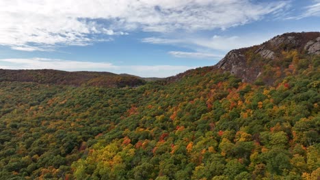 An-aerial-view-over-the-mountains-in-upstate-NY-during-the-fall-foliage-change,-on-a-beautiful-day-with-white-clouds