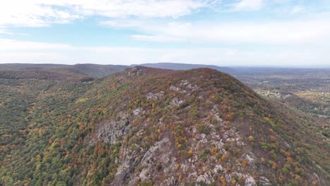An-aerial-view-high-over-Storm-King-Mountain-in-upstate-NY-during-the-fall-foliage-change,-on-a-beautiful-day-with-white-clouds