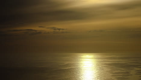 Goldene-Reflexionen-Auf-Der-Meeresoberfläche-Und-Wolken,-Die-Sich-Im-Gelben-Himmel-Bewegen