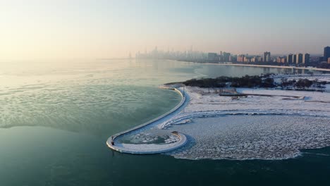Aerial-view-over-ice-and-the-Montrose-Harbor-Beacon-and-pier,-foggy,-winter-sunrise-in-Chicago,-USA