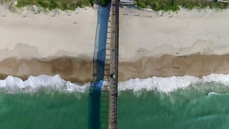 Top-down-aerial-view-of-the-Bogue-Inlet-ocean-pier-on-a-sunny-day,-four-times-speed