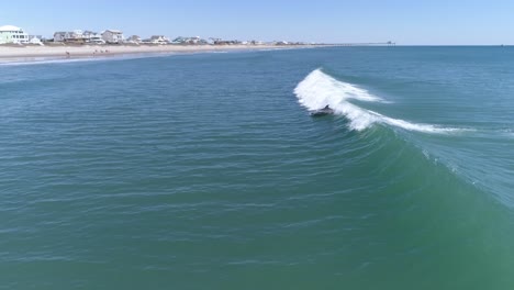 Dolphins-surfing-waves-together-along-North-Carolina-coast,-Aerial-Tracking-Shot