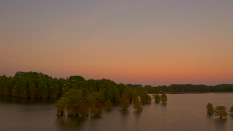 Höhenvideo-Eines-Wunderschönen-Sonnenuntergangs-Am-Stumpy-Lake-Virginia-Mit-Vögeln,-Die-Inmitten-Der-Bäume-Fliegen