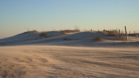 Heavy-winds-bury-a-fence-under-white-sand-dunes-during-a-sandstorm-in-the-day