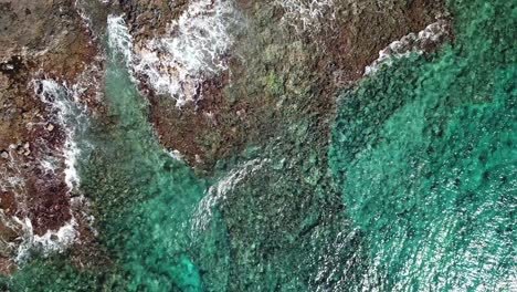 Drone-panning-shot-of-waves-hitting-the-beach-and-rocks-in-Kauai,-Hawaii-in-day