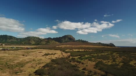 Drone-flying-away-from-inactive-volcano-over-golden-fields-in-Kauai,-Hawaii-on-sunny-day