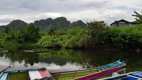 Colourful-small-boats-on-a-river-with-a-background-of-hills-in-Rammang-Rammang,-Makassar,-Indonesia