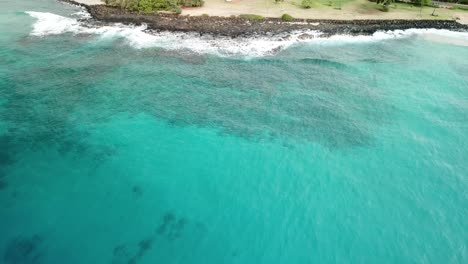 Drone-flying-over-ocean-towards-park-in-Poipu-in-Kauai,-Hawaii