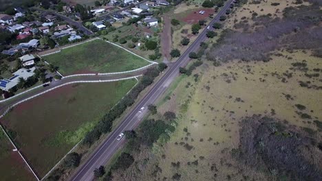Drone-tracking-white-trucks-on-road-in-Kauai,-Hawaii-and-revealing-mountains-in-the-distance-on-sunny-day