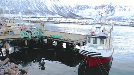 Fishing-boats-at-a-dock-of-a-northern-lake-and-mountains-covered-in-snow-in-winter-in-Tromso-Norway