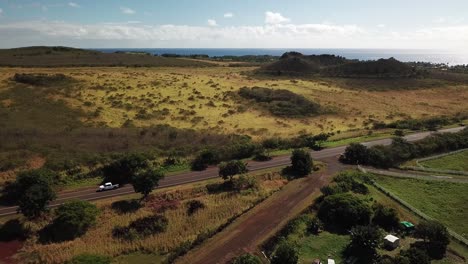 Drone-flying-towards-ocean-over-road-on-sunny-day-in-Kauai,-Hawaii