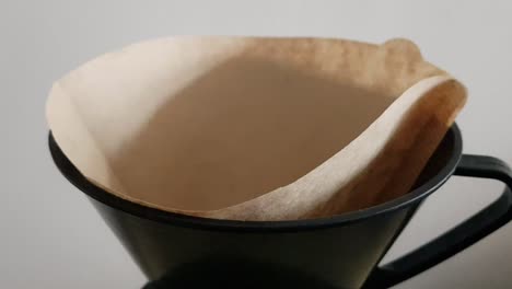 Metal-spoon-pouring-coffee-grounds-into-brown-coffee-paper-filter