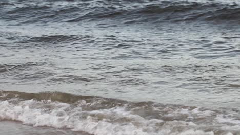 Close-up-waves-near-the-sea-shore-on-an-boring,-autumn-day-with-a-cold-and-chilly-weather-hitting-the-shore