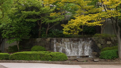 Tilt-down-revealing-a-lovely-autumnal-scene-with-a-small-waterfall-in-Ueno-Park,-Tokyo