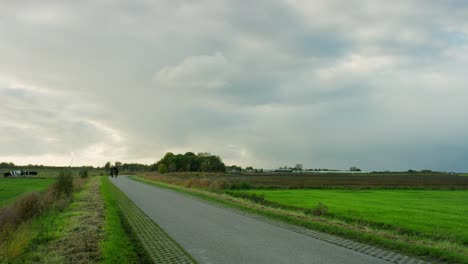 Two-people-riding-their-bicycle-in-the-distance,-on-a-rural-road-near-Middelburg,-the-Netherlands