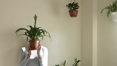 Female-person-hiding-face-behind-flowerpot-with-plant,static-medium-shot