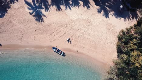 bringing-diving-bottles-and-diving-equipment-with-a-wheelbarrow-to-a-small-boat-on-a-tropical-sand-beach-in-Africa,-aerial-drone-shot