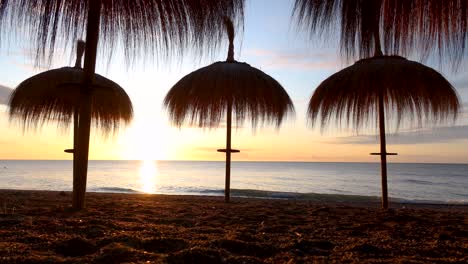 Timelapse-low-to-ground-on-beach-with-tropical-sun-umbrellas-on-marbella-beach-at-sunrise