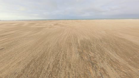 Drone-flying-towards-the-sea-at-an-empty-sand-beach,-flying-by-a-playground-in-Vrouwenpolder,-the-Netherlands