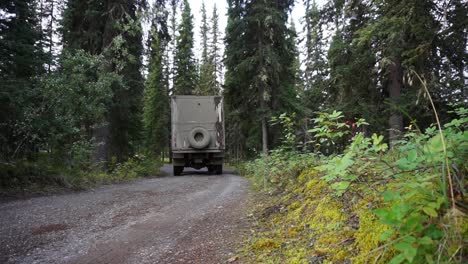 Static-low-angle-shot-of-a-large-off-road-truck-driving-through-a-spruce-forest-near-Eagle,-Alaska