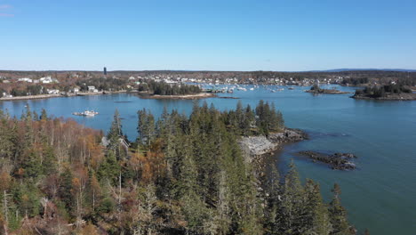 Aerial-Fly-Over-Drone-Footage-over-tree-foliage-revealing-Maine-Coast-Coastline-with-sprawling-parked-boats-at-Vinalhaven,-Fox-Islands,-Knox-County,-Maine,-USA