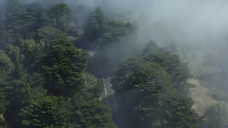 Aerial-Drone-Shot-over-Curved-Mountain-Road,-Couple-Cars-go-by-then-Drone-Moves-Forward-Over-Misty-Forest-with-Tilt-up-to-Reveal-Reservoir-and-Highway-in-Background