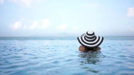 Woman-with-striped-sun-hat-in-swimming-pool-looking-away-from-camera