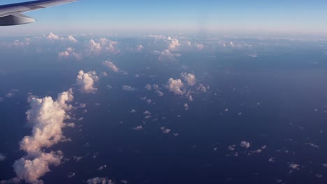 Window-view-of-an-airplane-wing-flying-above-the-small-white-clouds-and-wide-blue-ocean-traveling-to-Azerbaijan